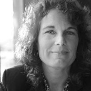 A Caucasian women with curly hair shown in a black and white photo, smiling straight at the camera.