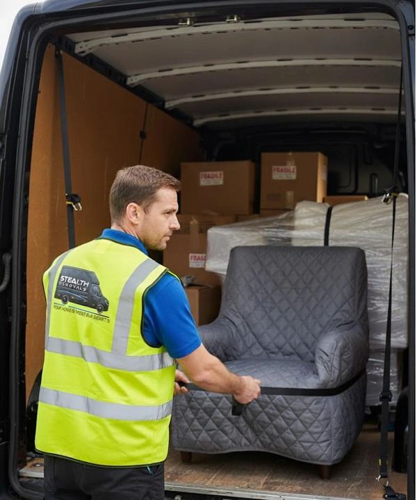 Mover securing a padded armchair inside a van with fragile boxes in the background.