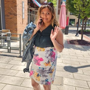 Woman smiling and waving while on phone outdoors.