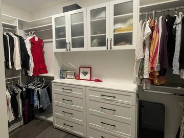 Organized walk-in closet with white cabinetry and hanging clothes.