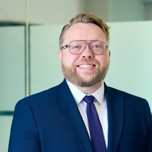 Smiling man in a blue suit and glasses in an office setting.
