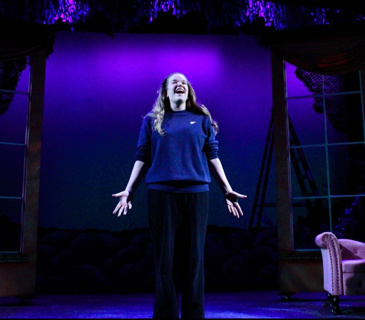 Person joyfully performing on stage under purple light.
