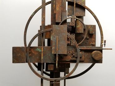 Abstract rusty metal sculpture with geometric shapes and circles on a white background.