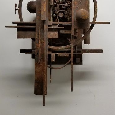Rusty geometric metal sculpture with intersecting shapes on a plain wall.