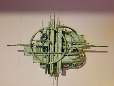 Abstract green metal sculpture with geometric shapes and circles.