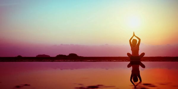 Person meditating by calm water during sunset with reflection.