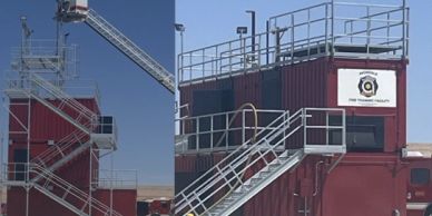 Red training tower with metal staircases and safety railings under clear sky.