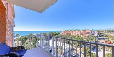 Balcony view overlooking the ocean with seating and nearby buildings.