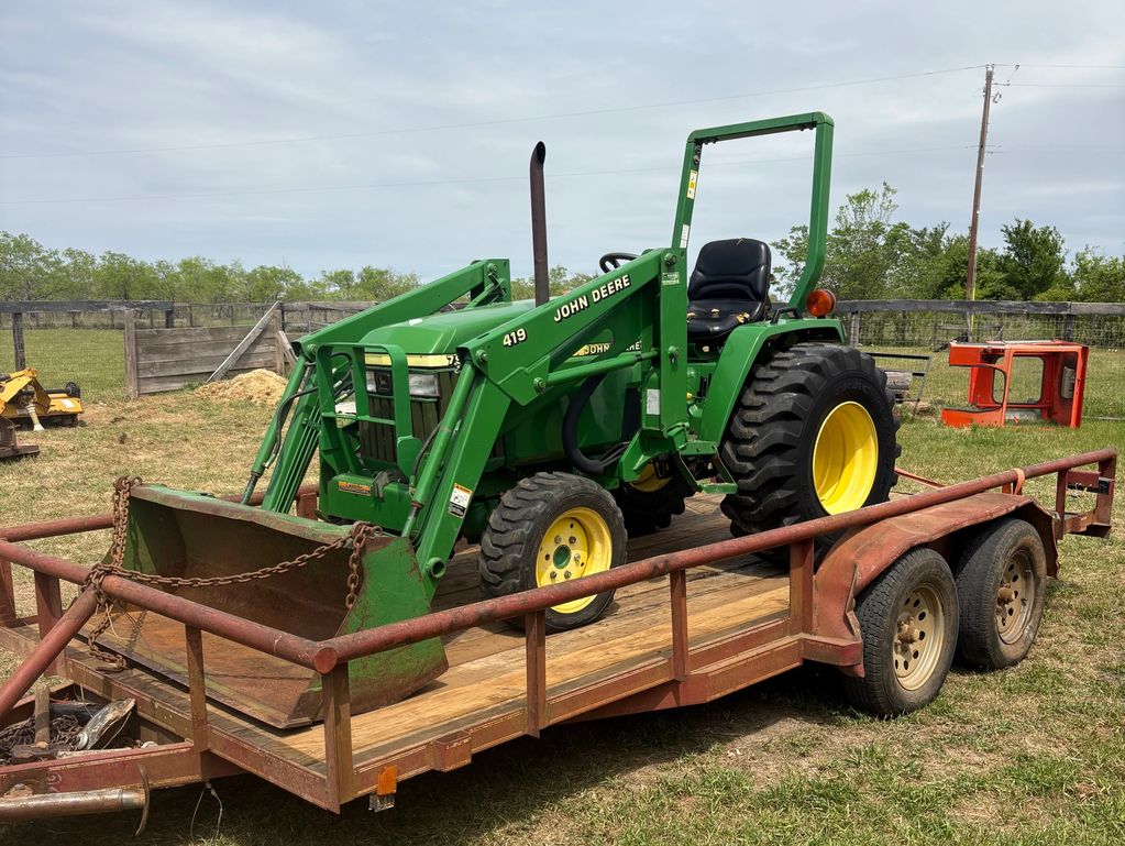 Green John Deere tractor on a rusty trailer in a grassy yard.