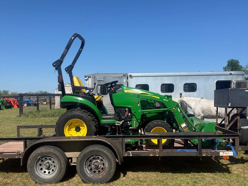 Green John Deere tractor loaded on a trailer under clear blue sky.