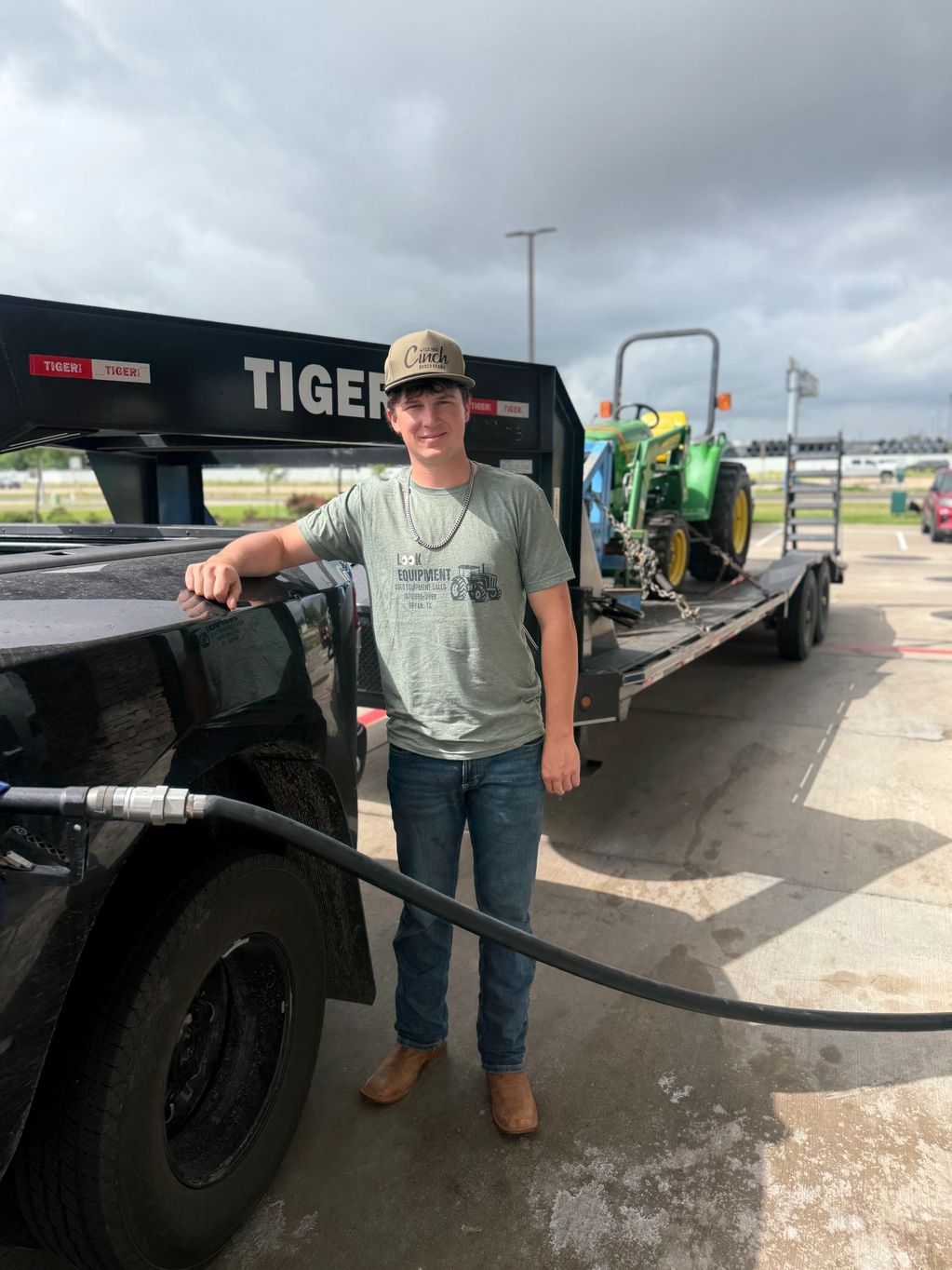 Young man fueling a truck with a tractor on a trailer in the background.