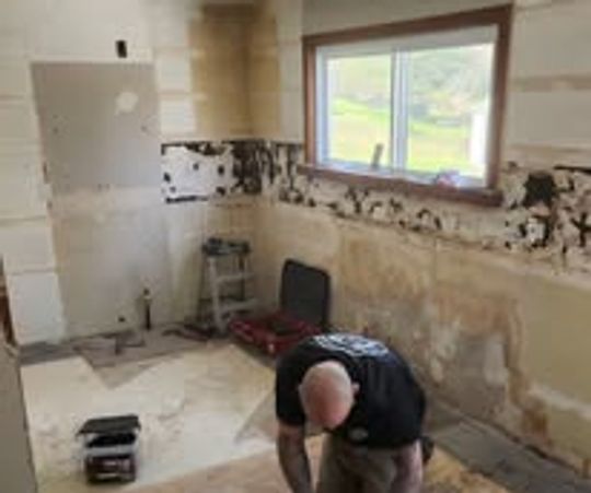 Man remodeling a kitchen with stripped walls and removed cabinets.