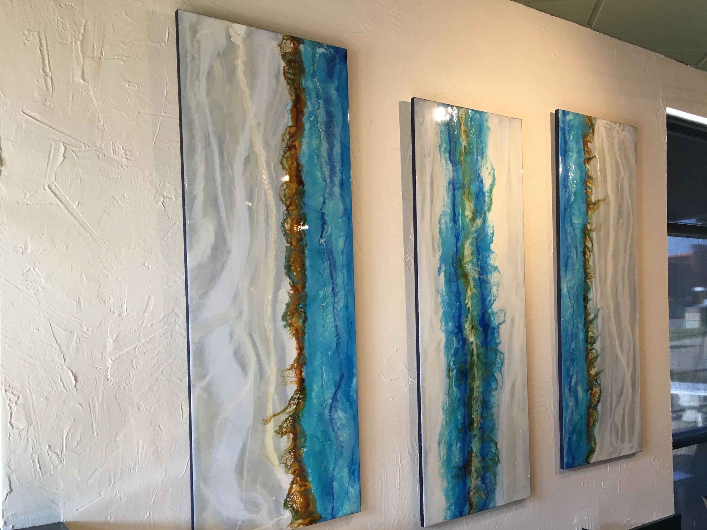 3 white and blue ocean paintings hanging vertically in a restaurant