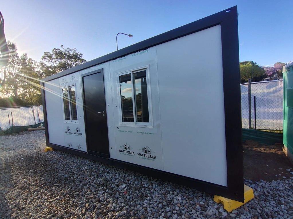 A modular portable building unit on a gravel surface under clear skies.