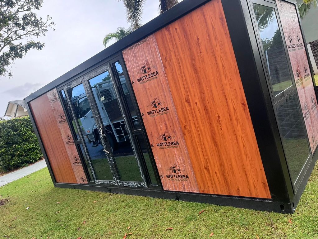 A modular building unit with wood paneling and glass doors on grass.