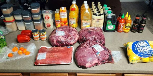 A variety of meats, spices, sauces, and condiments arranged on a kitchen counter.