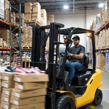 Worker operating a forklift moving shoe boxes in a warehouse.