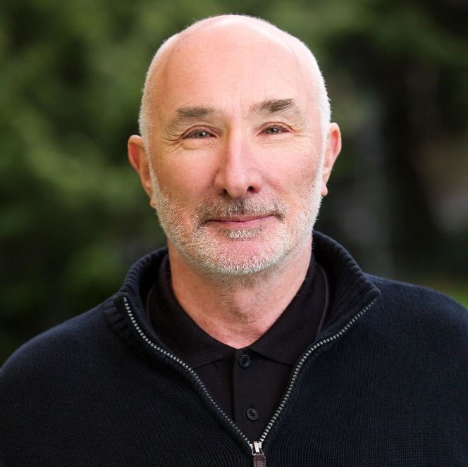 Smiling bald man with light facial hair in outdoor setting.