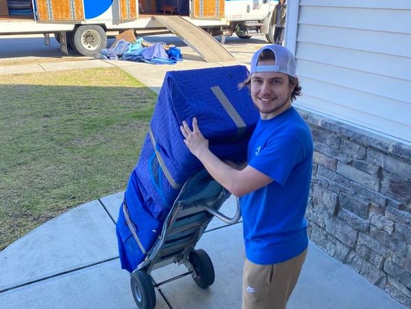 Mover dollying furniture into a customer's house and smiling