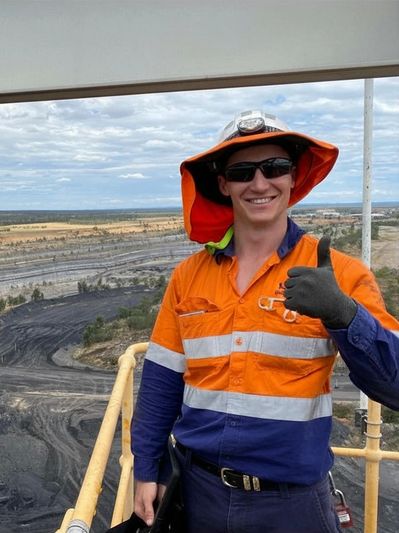Worker in orange safety gear gives thumbs up at mining site.