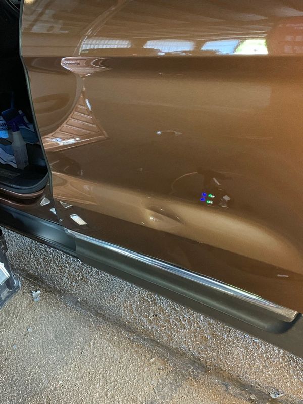 Brown car door with a big crease dent near the bottom.