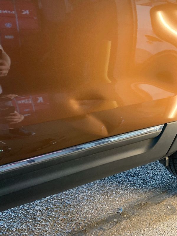 Big dent on the side of a brown car door near the bottom trim.