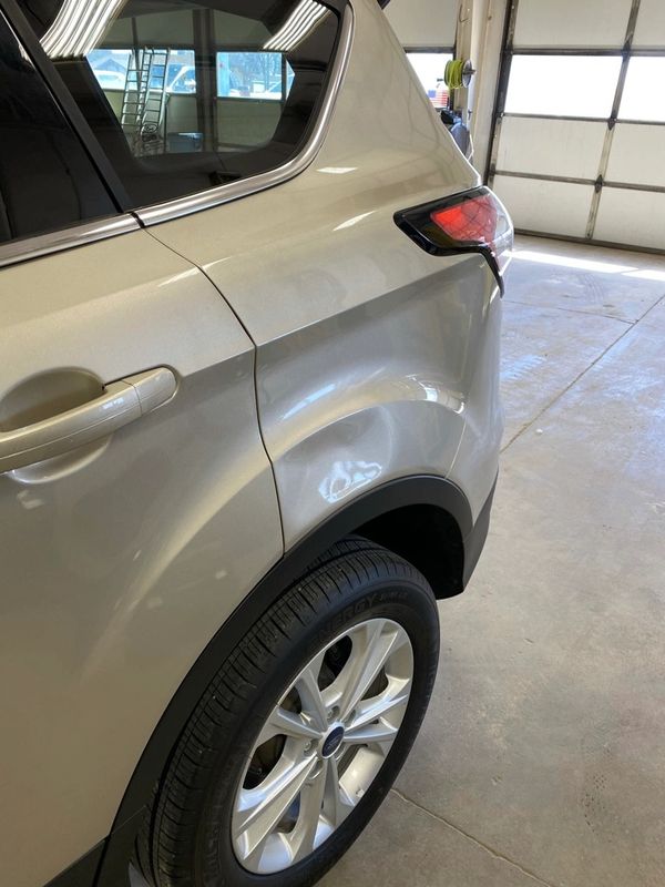 Dent on the rear driver side quarter of a beige SUV.