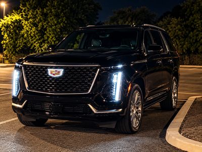 Black Cadillac SUV parked at night with lights on.