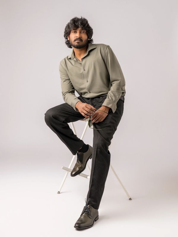 Man wearing a green shirt and black pants sitting on a white stool.