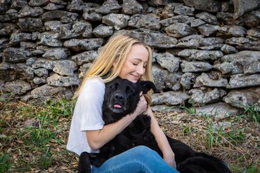 Austin pet photography portrait of woman hugging black dog by stone wall