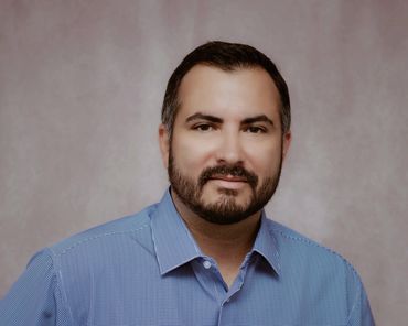 Professional headshot of Austin businessman in blue shirt on studio gray background