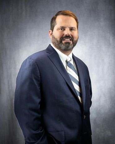 Professional headshot of Austin businessman in navy suit on studio gray background