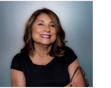 Studio headshot of Austin woman in black top with friendly smile on soft blue gray backdrop