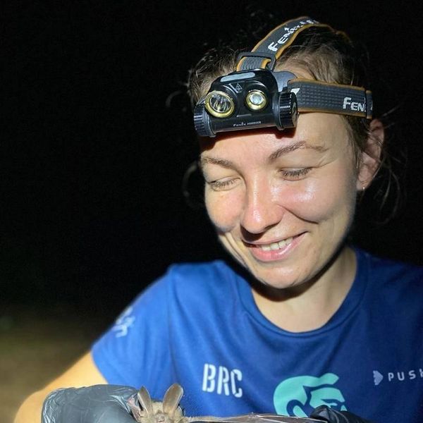 Woman wearing a headlamp smiles while holding a bat at night.