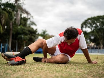 A soccer player in a red jersey and shorts sits on grass