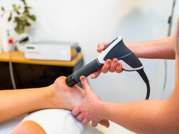 A therapist uses a handheld treatment device on a patient's foot during a therapeutic