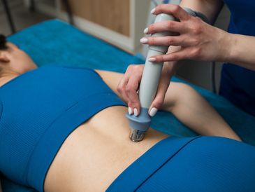 A person wearing a blue outfit receives treatment on their lower back with a therapy device