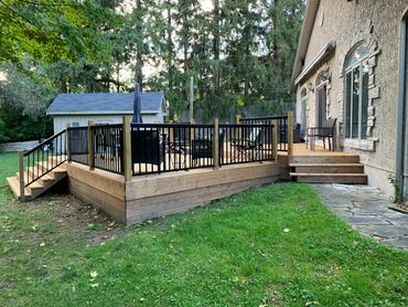 A spacious wooden deck with black railings and outdoor furniture attached to a house.