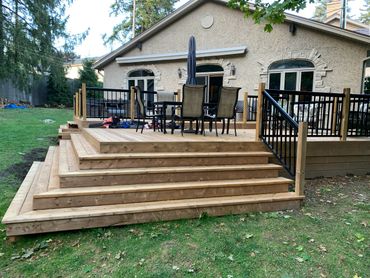 Spacious wooden deck with black metal railings and outdoor furniture.
