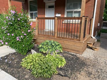 Front porch with wooden railing and lush green plants.