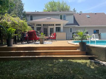 Person relaxing on a red chair by a backyard pool on a sunny day.