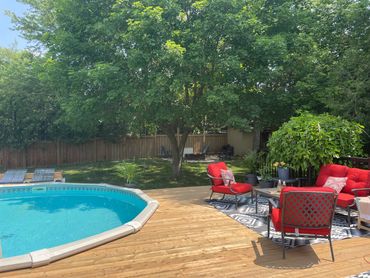 Backyard with pool, red outdoor furniture, and large tree providing shade.