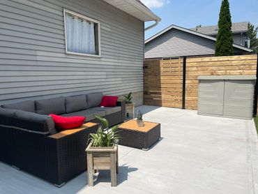 Modern backyard patio with grey wicker furniture and red cushions under clear sunny skies.