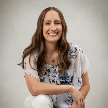 A smiling woman with long brown hair, wearing a floral blouse.