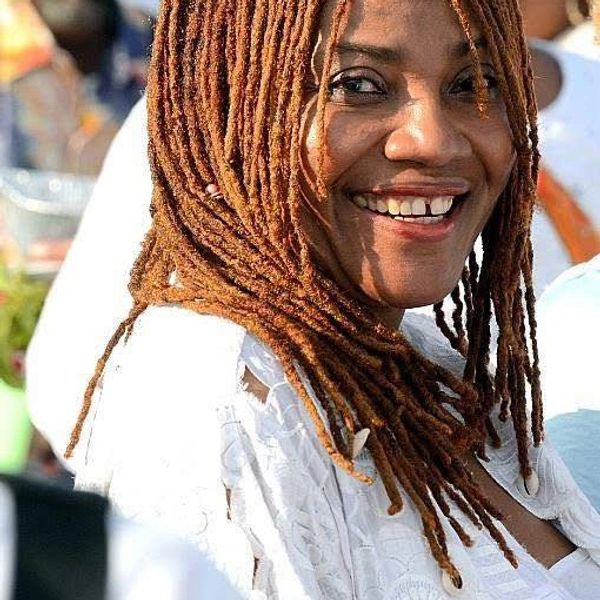 Smiling woman with long auburn dreadlocks wearing a white outfit outdoors.
