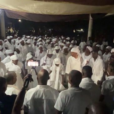 A large group of people dressed in white gathered at night under a canopy.