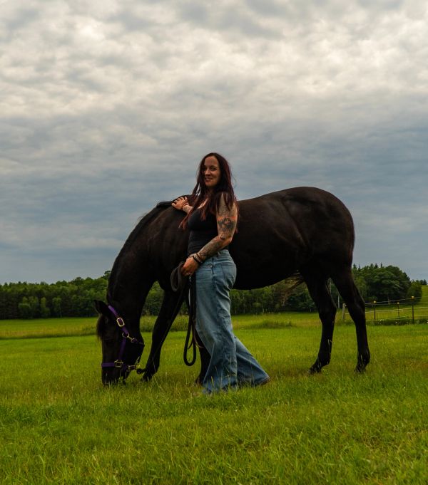 Woman standing next to a black horse in a grassy field.