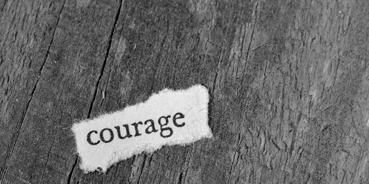 A torn paper with the word 'courage' on a wooden surface.