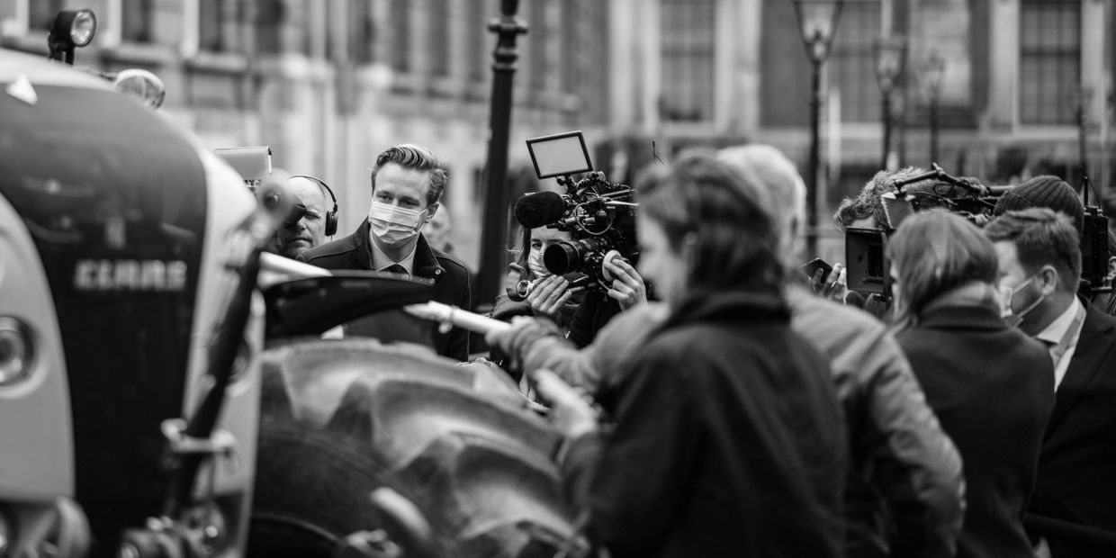 Journalists and cameramen filming an event involving a tractor outdoors.