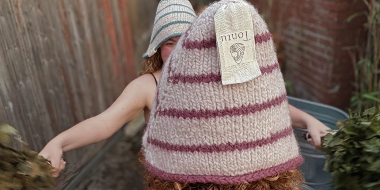 Person wearing knitted hat with label, holding branches.